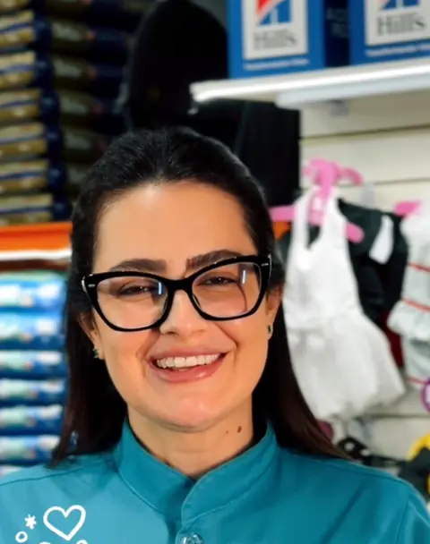 Profissional de óculos e uniforme turquesa sorrindo na loja